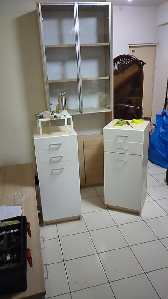 1) 照片顯示一個房間裡有三個白色的櫃子,一個玻璃門的櫃子在左邊牆上,兩個櫃子在中間,一個木頭櫃子在右邊牆上