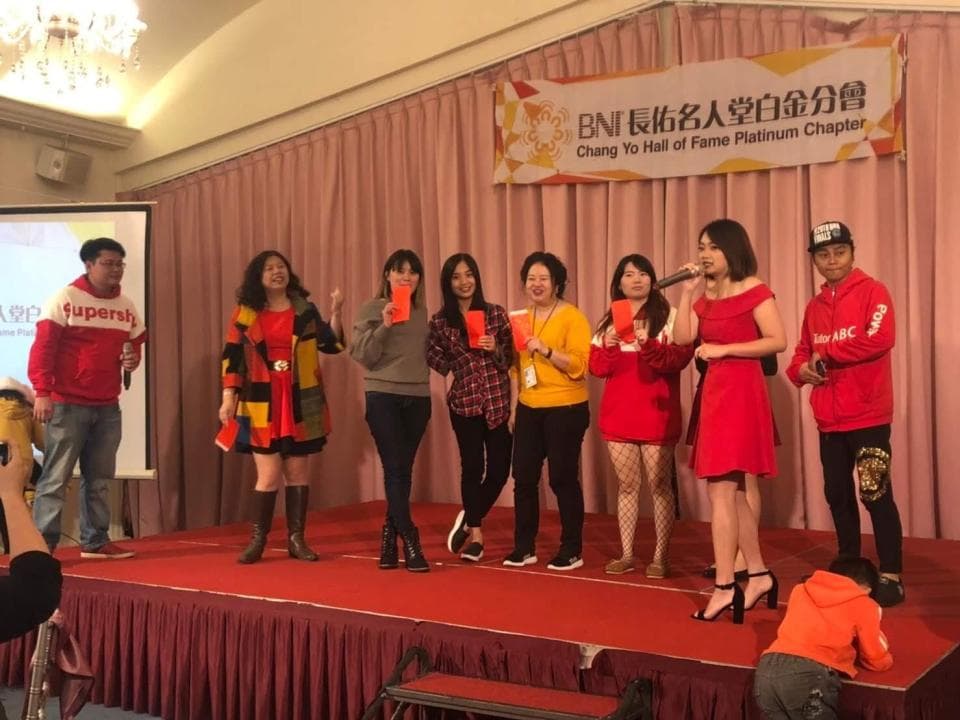 這張照片是 BNI 俱樂部名人堂白金分會的活動照片。照片中,一群人站成一排,其中一名女士正在唱歌,其他人在觀看或微笑。