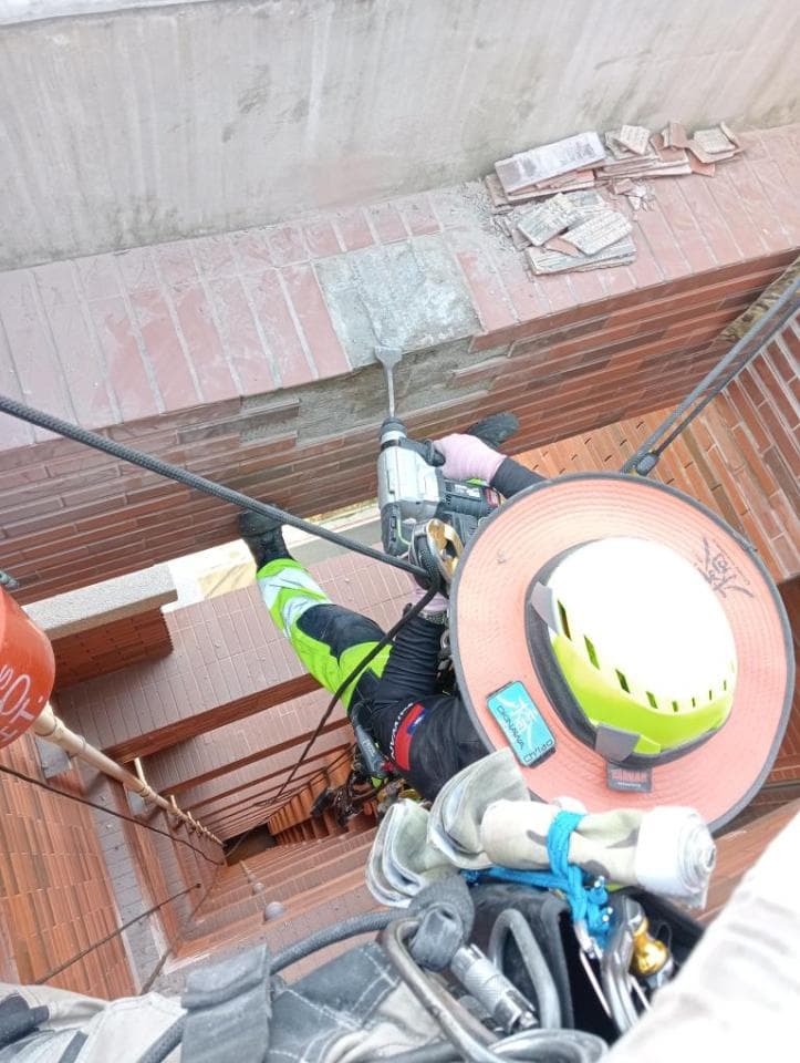 1. 照片中顯示一位身穿安全裝備的工人正在高處作業,使用電鑽破壞牆壁