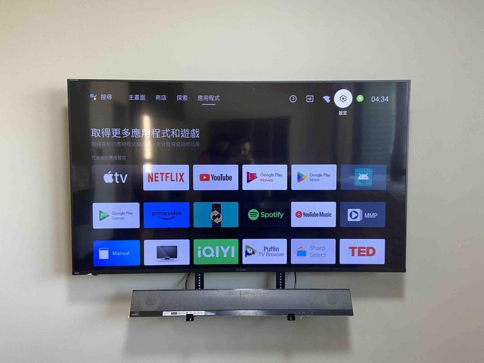 這張照片是一台安裝在牆上的電視,電視下方有一個黑色條狀的音響,電視屏幕上顯示着各種流媒體服務的應用程式圖示。