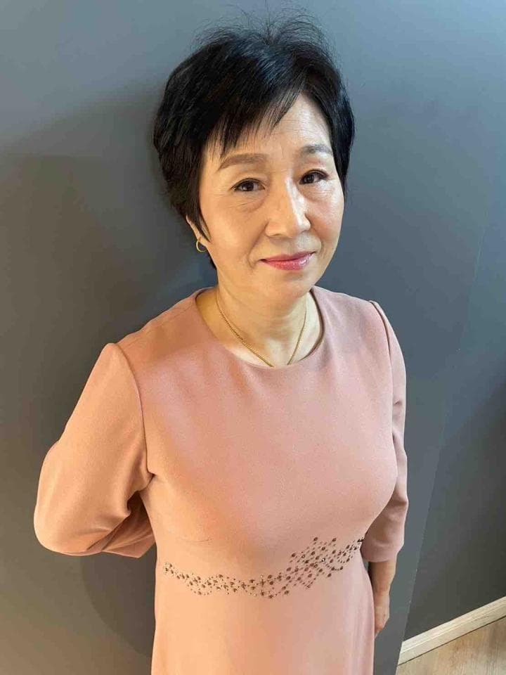 這張「一位女士」的照片是,她留著黑色短髮,穿著粉紅色連衣裙,上面有黑色圖案。