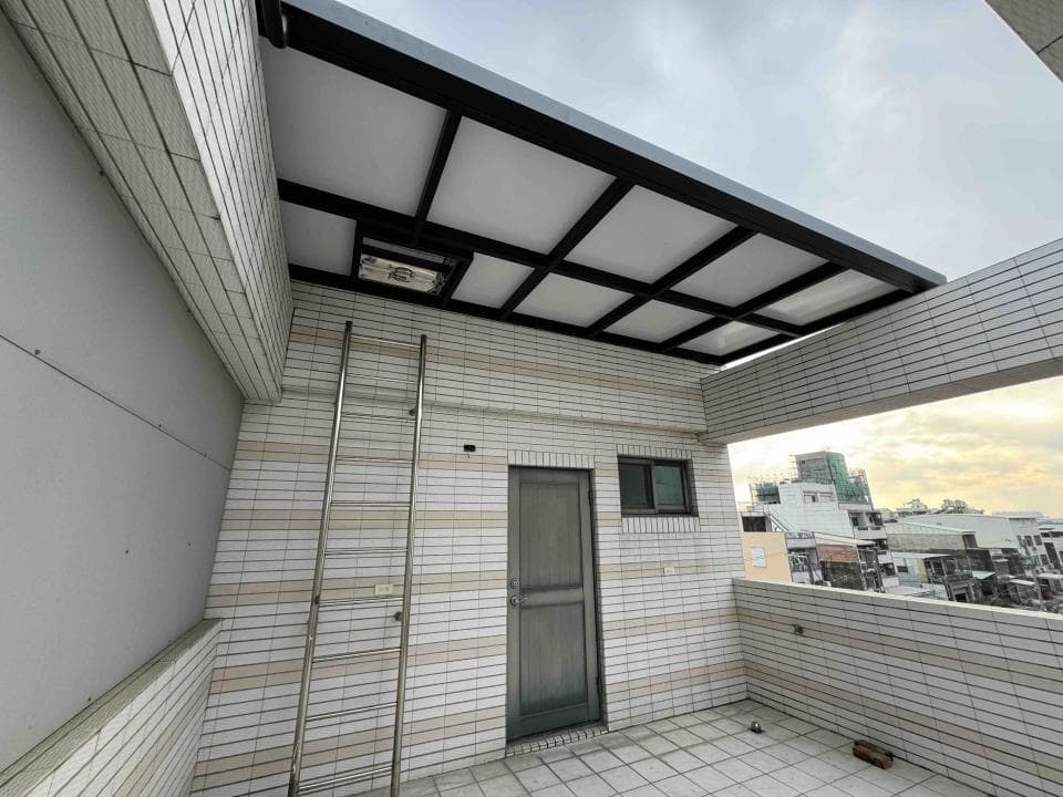 這張「陽臺」的照片是一個帶有現代化遮陽棚的陽臺,陽臺牆壁採用白色磚塊,並有一個金屬梯子。