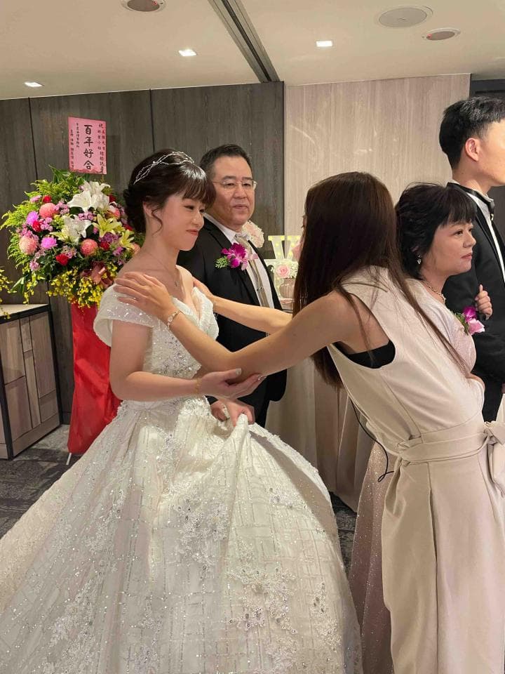 這張照片是一個婚禮現場,新郎和新娘正在擁抱,新郎的父親和新娘的伴娘也一起在場,場面溫馨幸福。