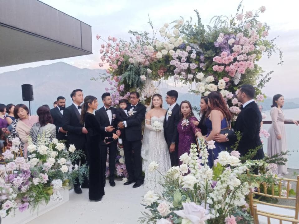 這張「婚禮」的照片是一個戶外婚禮,新娘穿著婚紗,新郎穿著西裝,他們站在花拱門下,旁邊站著他們的家人和朋友。