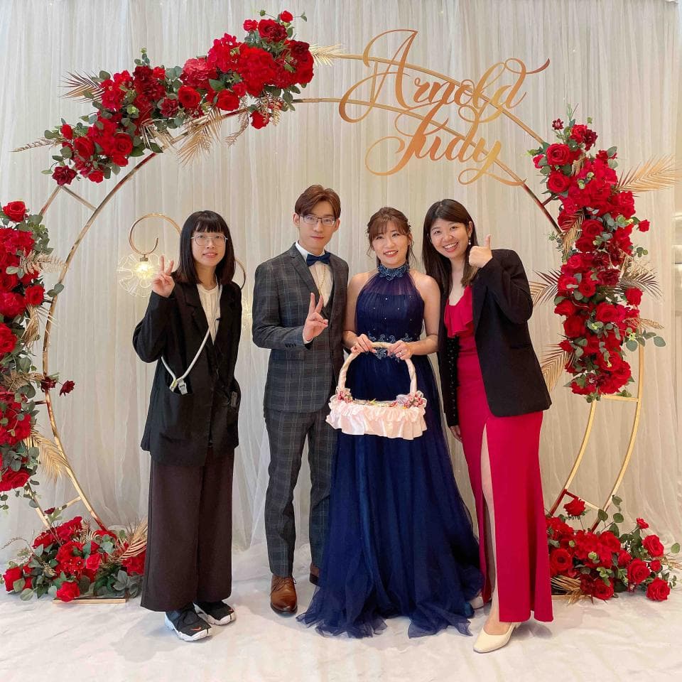 這張「婚禮」的照片是 一對新人和他們的伴郎伴娘,他們站在一個佈置滿鮮花的拱門前。新郎穿著西裝,新娘穿著藍色的禮服。