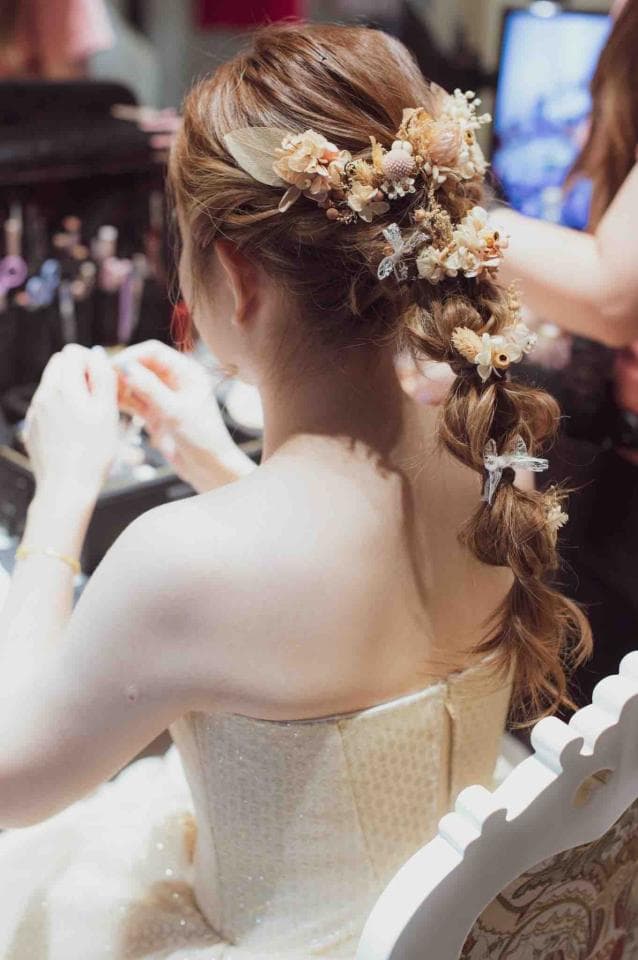 這張「新娘準備婚禮」的照片是一個穿著白色禮服的新娘,她的頭髮編了辮子,並用乾燥花裝飾。