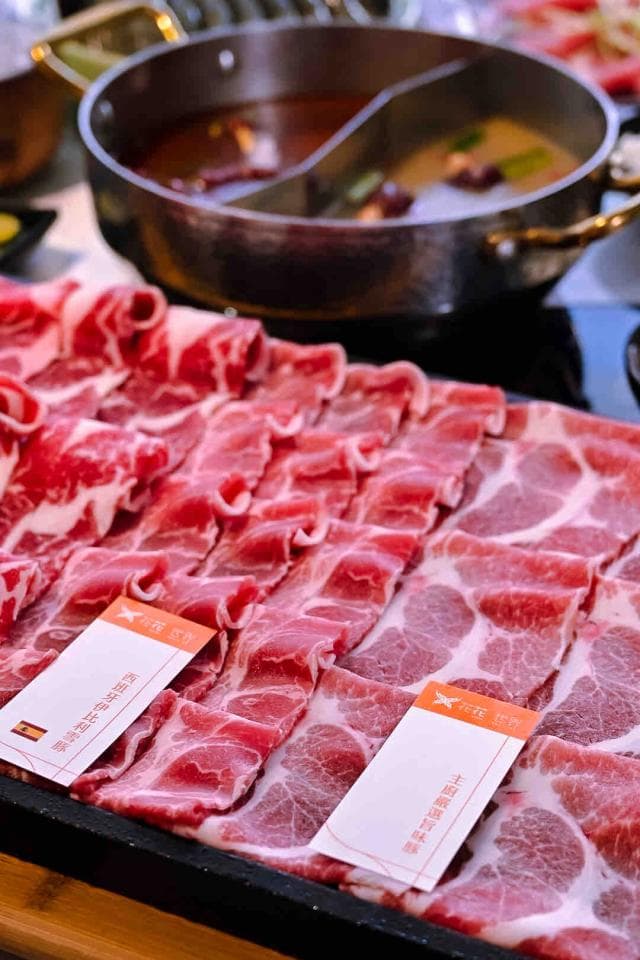 這張「火鍋肉片」的照片是擺放在盤子上,上面有牛肉和豬肉,旁邊有一鍋麻辣湯底。