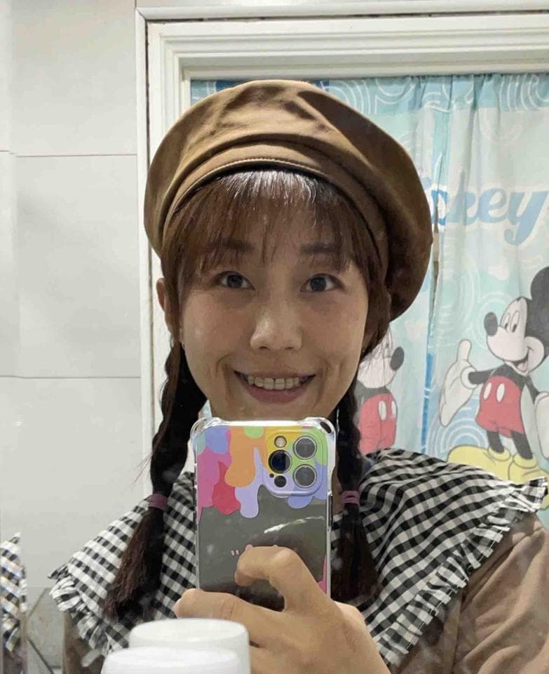 這張照片是一個年輕女性的自拍照,她戴著一頂棕色貝雷帽,穿著一件格紋襯衫,並手持一部手機。