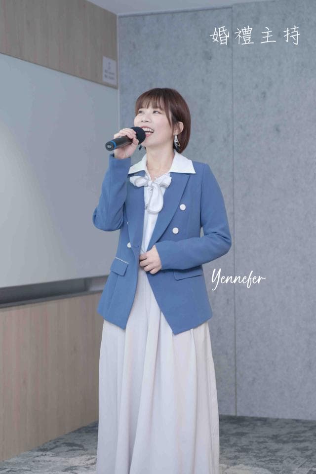 這張「女性演講」的照片是一個穿著藍色外套和白色裙子的女人,她正在拿著麥克風演講。