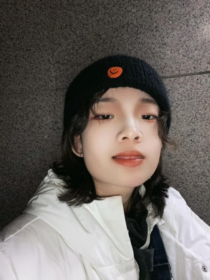 1) 照片中是一位年輕女性,她戴著黑色毛線帽,穿著白色外套,站在灰色牆壁前