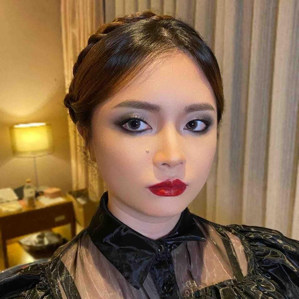 這張照片是一個年輕女性的肖像,她戴著黑色的眼影和紅色的口紅,頭髮編成了辮子。