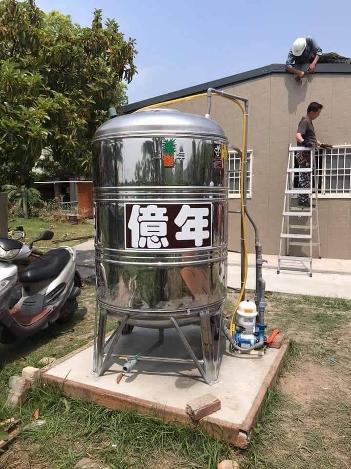 1) 照片中展示了一個大型的不銹鋼水箱,安裝在水泥基座上,並配備了水泵和管道系統