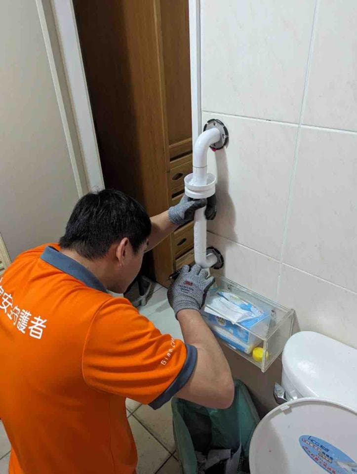 1) 照片顯示一位身穿橘色工作服的男性,正在浴室裡修理馬桶排水管