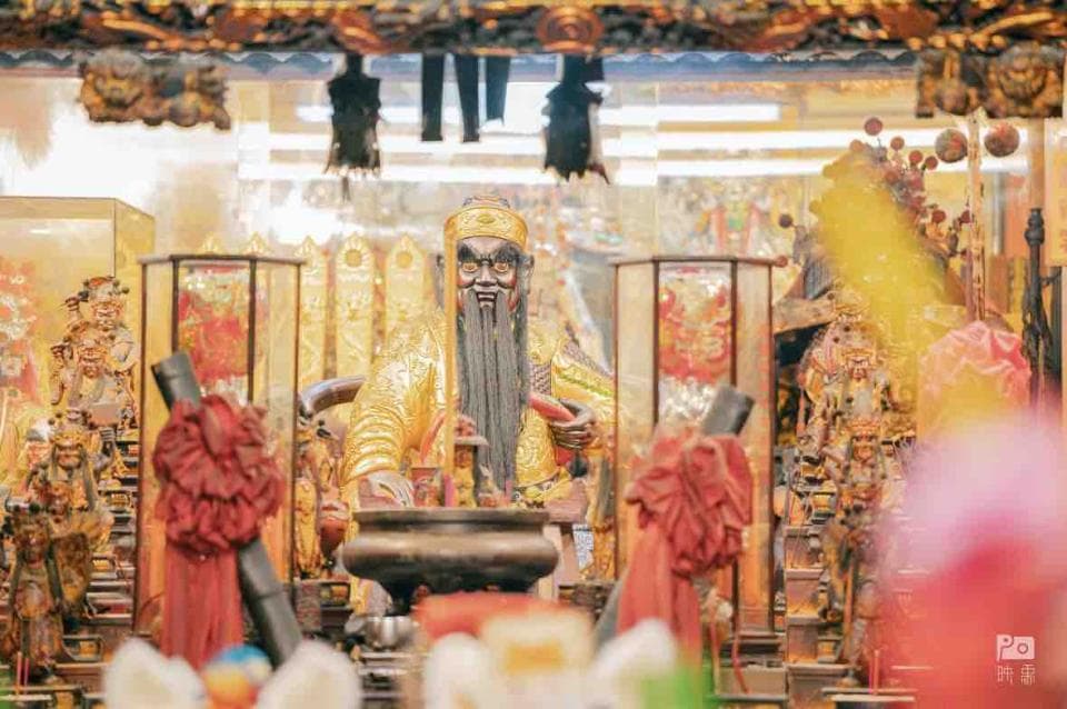 1) 照片顯示了一個金色的雕像,雕像是一個有鬍鬚的男性,頭上戴著皇冠,雕像在一個紅色和金色的裝飾中