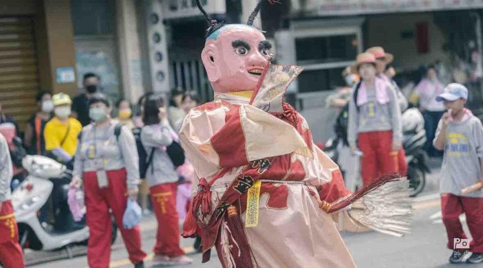 這張「神明遶境」的照片是,一群人跟著神明遊行,神明穿著華麗的服飾,手持法器,神情莊嚴。