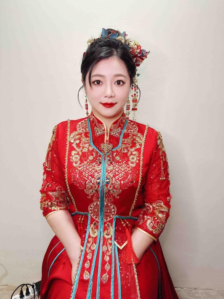 這張照片是一位穿著紅色旗袍的女性。她頭上戴著精緻的頭飾,臉上化著淡妝,看起來很優雅。她的旗袍上繡著精美的圖案,增添了華麗感。