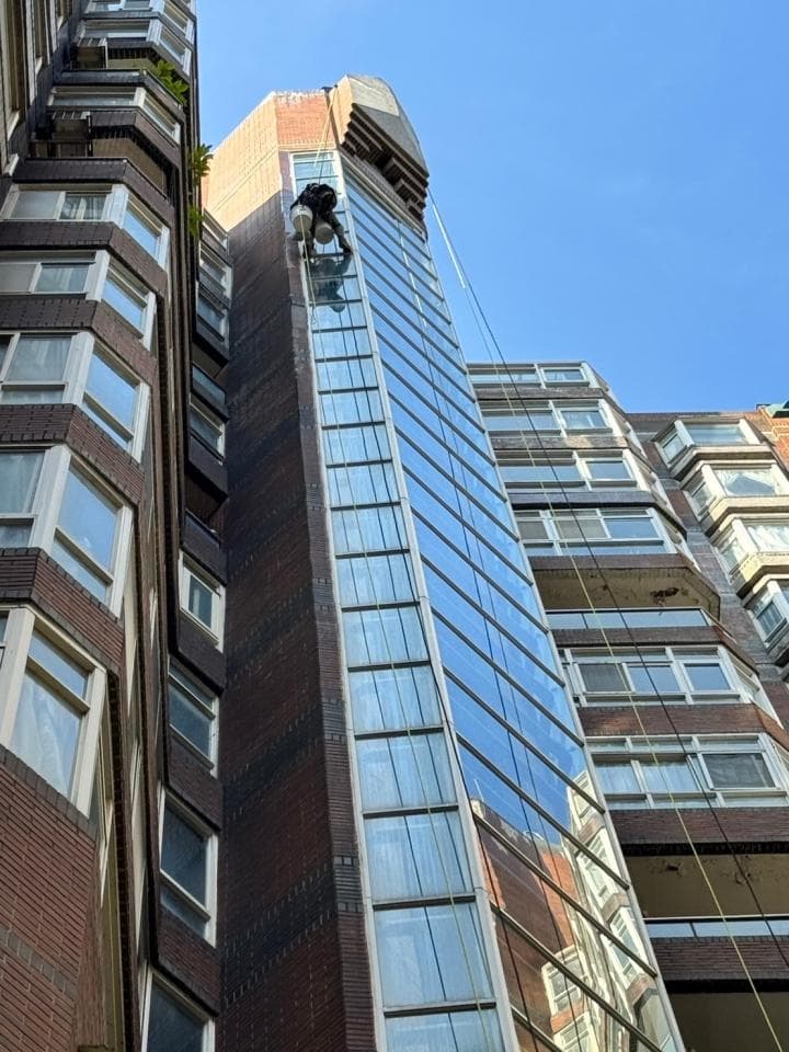 1) 照片顯示一座高聳的建築物,工人利用繩索懸掛在建築物的窗戶外清洗玻璃