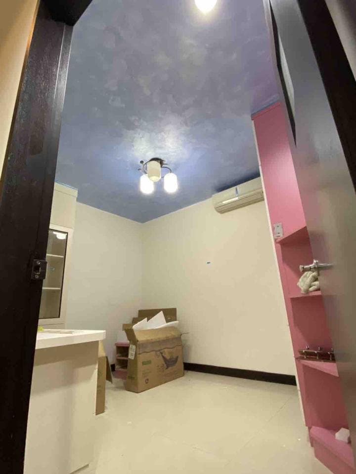 1) 照片顯示一個空房間,房間裡有一張白色桌子、一個紙箱和一個粉紅色的書架