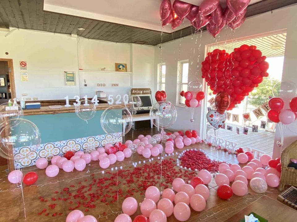 這張照片是一間佈置浪漫的房間,裡面放滿了氣球和玫瑰花瓣,還有用紅色氣球做成的愛心,非常適合求婚或慶祝情人節。
