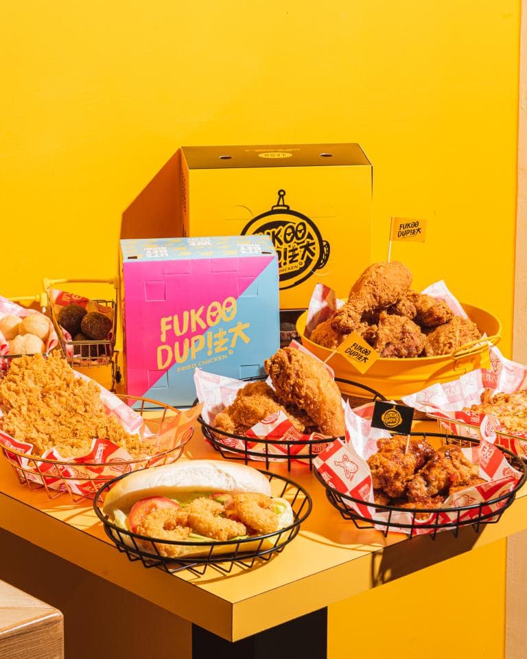 這張「炸雞」的照片是一個黃色的背景,上面擺放著各種炸雞和炸雞相關的包裝盒,以及擺放炸雞的籃子。