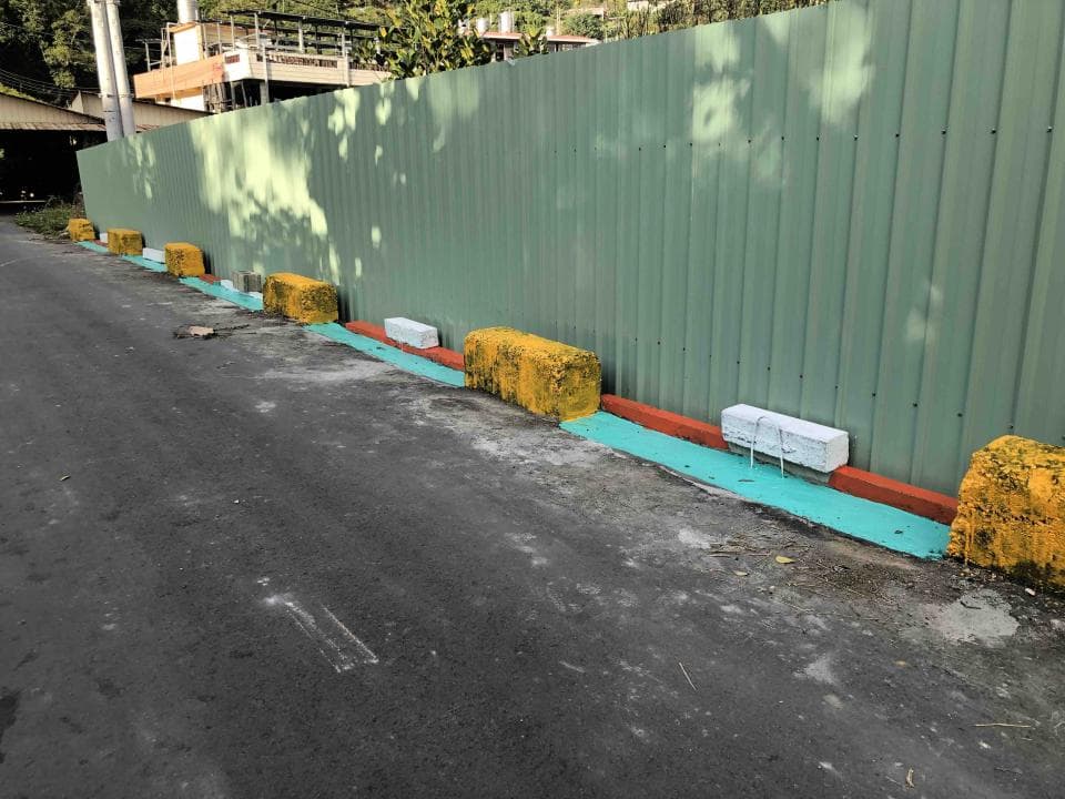 這張照片是一條水泥路,路邊有一排黃色的水泥塊,水泥塊之間以藍綠色的油漆做區隔,還有一條紅色的油漆線。