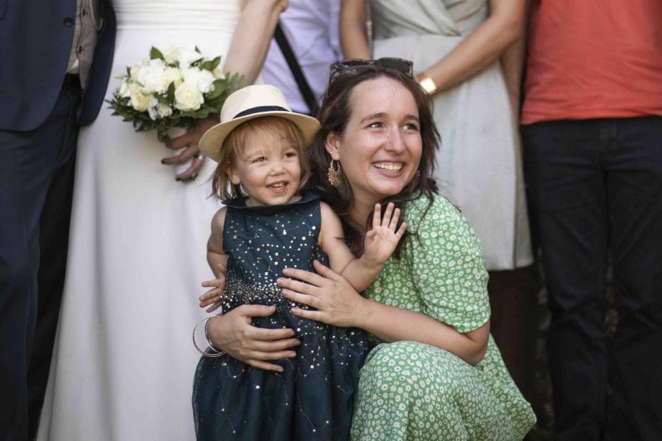 這張照片是一個女人抱著一個穿著藍色洋裝的小女孩,她們的背景是一群人。