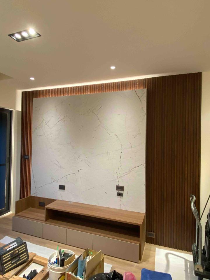 1) 照片展示了一個裝潢完畢的客廳,牆上貼著白色大理石紋路的磁磚,並搭配木紋壁板,下方設置木質電視櫃,空間整體簡潔明亮