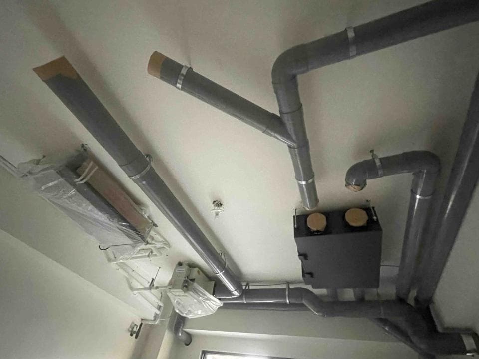 1) 照片顯示一個天花板,上面有許多灰色管線和一個黑色的箱子