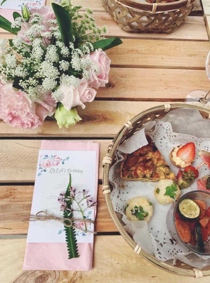這張照片是一個精緻的野餐,照片最重要的部分是一張粉紅色的卡片,上面寫著「It's Birthday」和一些花卉圖案。