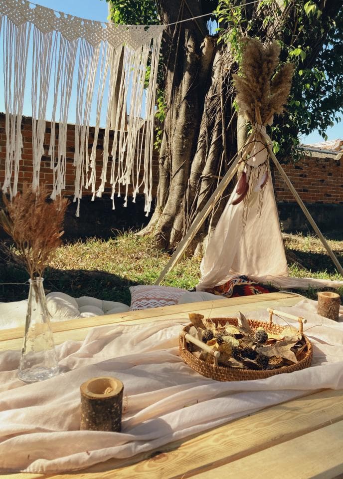 這張「戶外野餐」的照片是一張木製桌子上鋪著白色布,擺著一個裝滿食物的藤編籃子的照片,背景是一棵大樹和白色的蕾絲布。