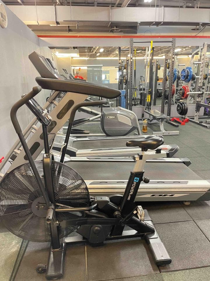 這是一張健身房的照片,裡面有跑步機和風阻腳踏車。風阻腳踏車可以幫助你鍛鍊心肺功能、增強肌肉力量和燃燒脂肪。想找風阻腳踏車的教練?快上PRO360!