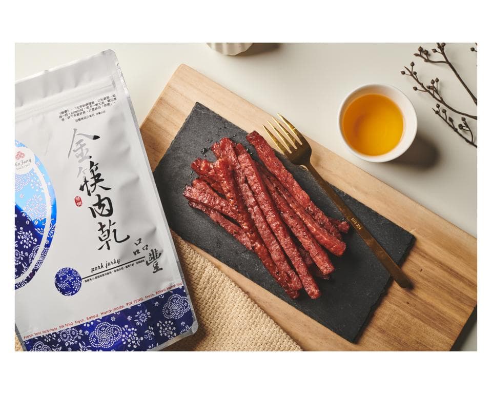 這張「肉乾」的照片是一包肉乾,上面有中文標籤,旁邊放了一盤肉乾和一杯茶,看起來很美味。