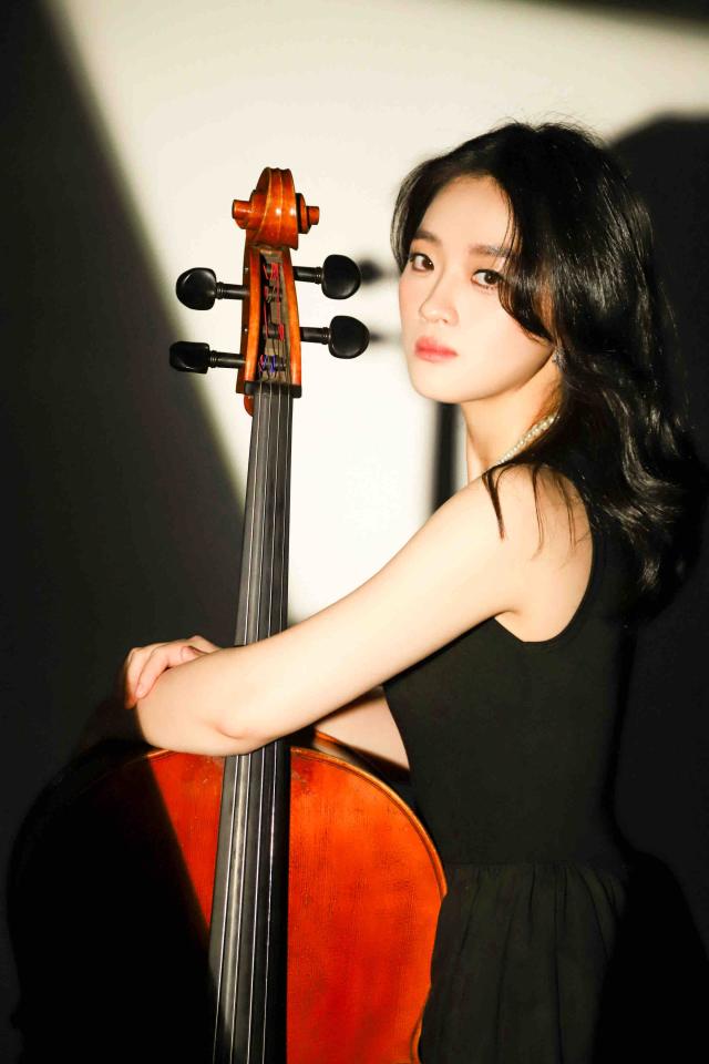 這張照片是一個年輕女性手持大提琴的照片,她身穿黑色連身裙,眼神堅定,表現出對音樂的熱愛。