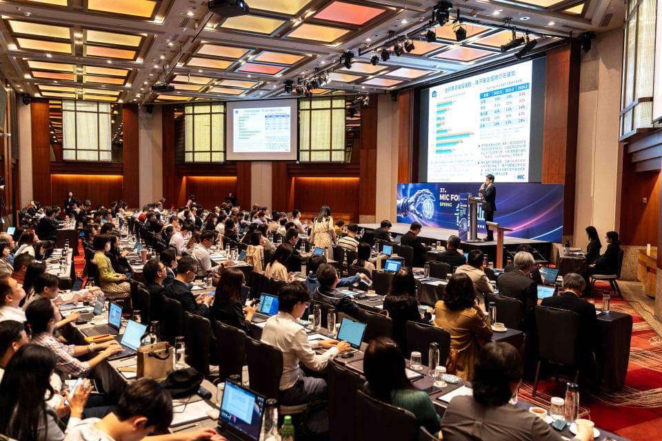 這張照片是一個大型會議室,裡面坐滿了聽眾,講臺上有個演講者正在演講,現場畫面非常熱鬧。