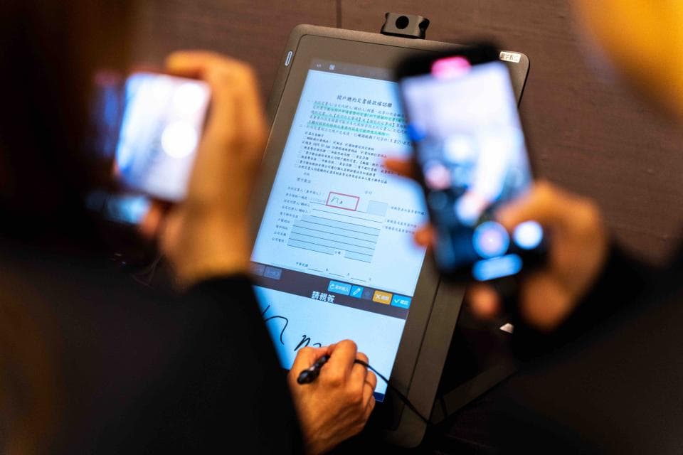 這張照片是一個人在使用電子簽名平板電腦簽署文件。平板電腦上有顯示的文件,而該人正在用手指簽署文件。