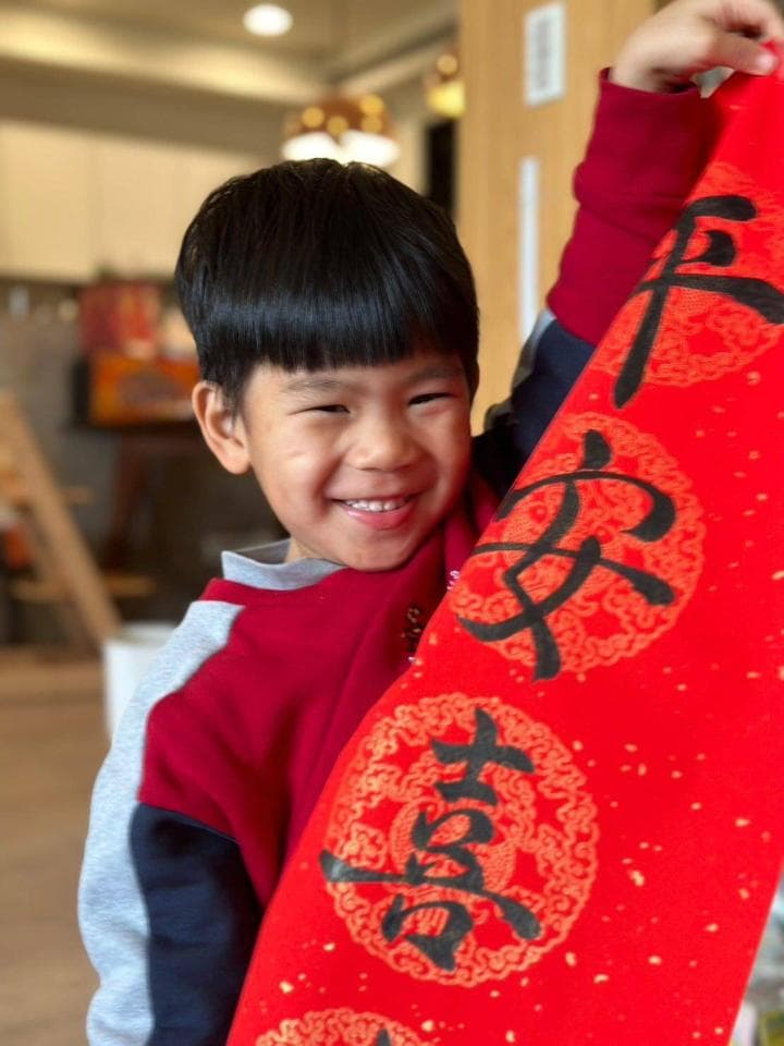 這張「一個小男孩手拿著紅色春聯,笑得很開心」的照片是。