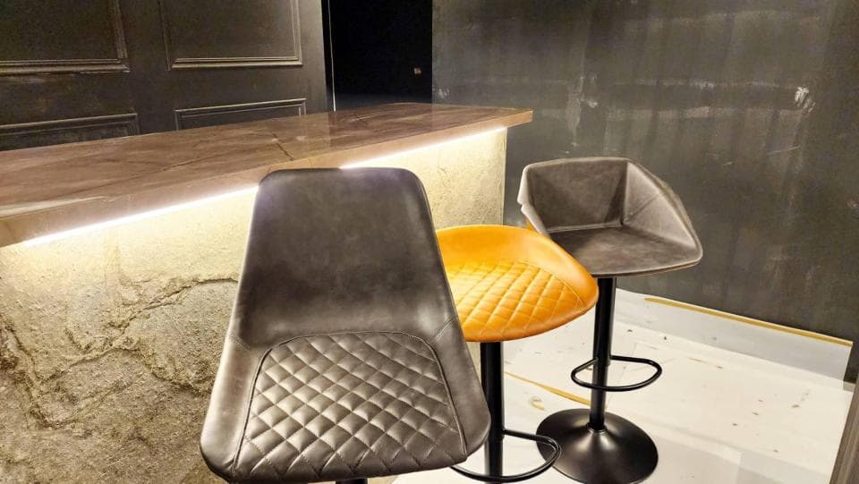 這張「吧檯」的照片是一個木製吧檯,上面有三個吧檯椅,其中兩個是黑色的皮革椅,另一個是黃色的皮革椅。