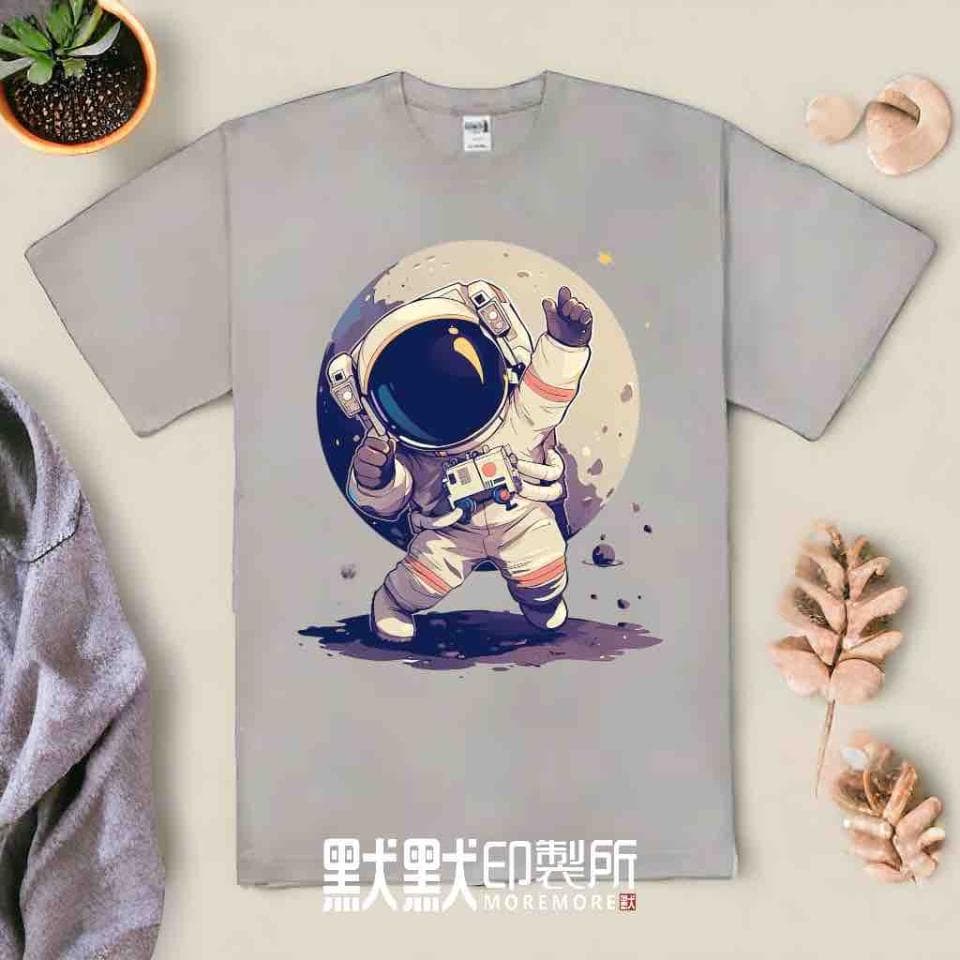這張照片是一件淺灰色的T恤,上面印著一個在月球上跳舞的太空人。太空人戴著頭盔,穿著白色的太空衣,雙手舉起,似乎正在跳舞。月球的背景是紫色的,上面有一些星星,營造出太空的氛圍。