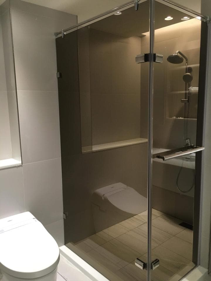 這張浴室的照片是一個淋浴間和馬桶的空間,淋浴間是玻璃門,馬桶是白色,背景是灰色磁磚。