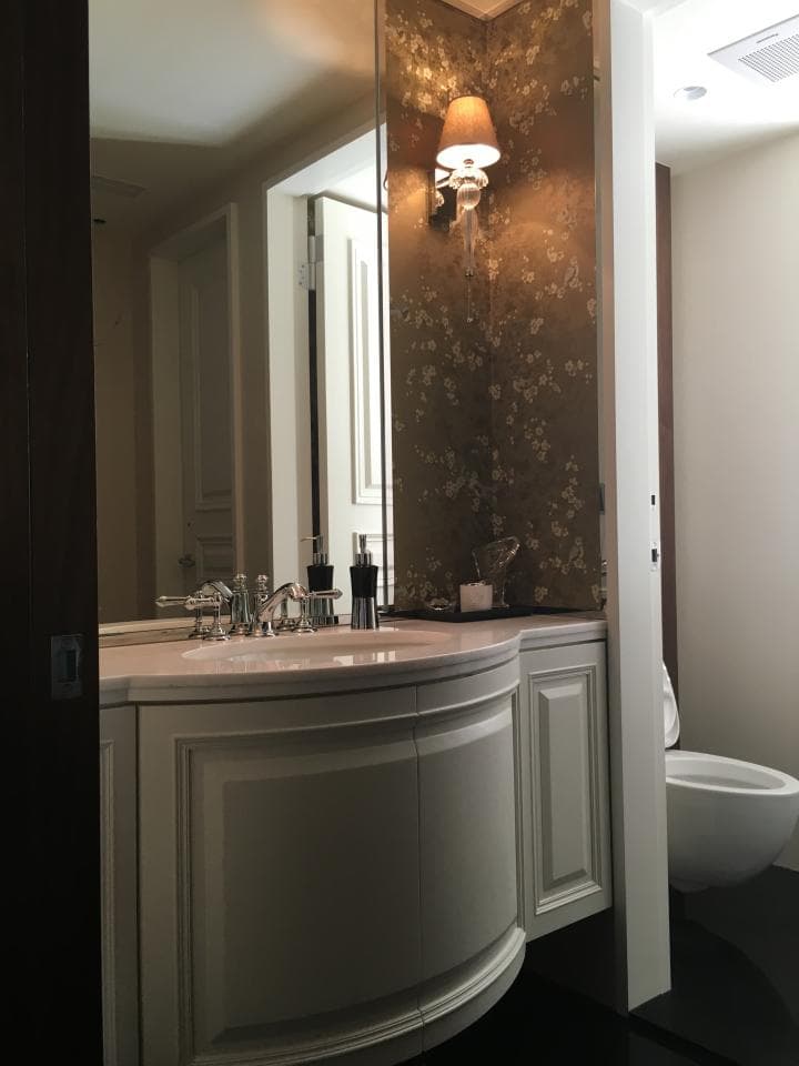 這張浴室的照片是一個帶有白色櫥櫃的現代化浴室,配有花卉圖案的壁紙和一盞壁燈。