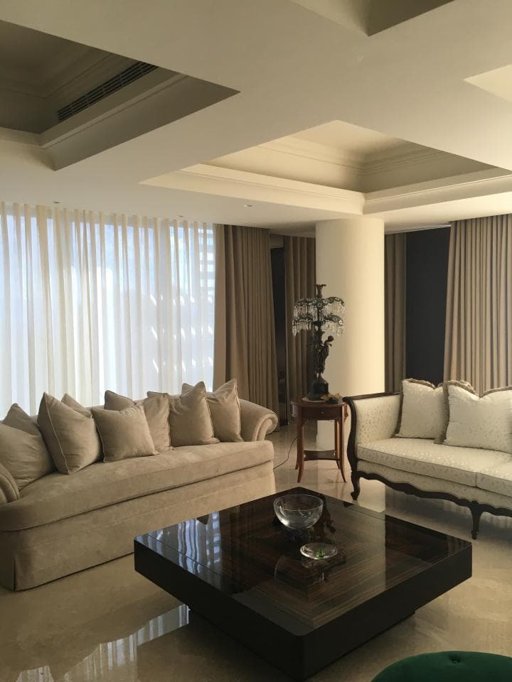 這張「客廳」的照片是一個現代化的客廳,有著淺色系的牆壁和沙發,中間擺放著一張黑色玻璃茶几,旁邊放著一個花瓶。