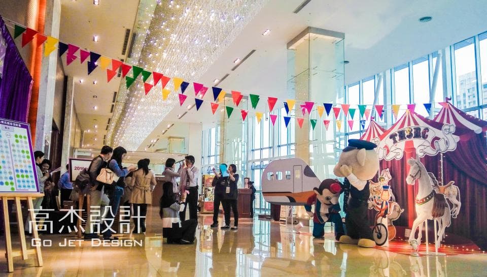 這張照片是大型的室內遊樂場,佈置的非常熱鬧,還有許多人來玩耍。最顯眼的是中間的舞臺,上面有可愛的卡通人物和一個小型的旋轉木馬。