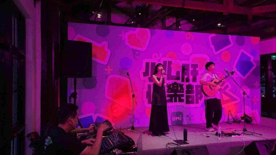 這張照片是一個小型音樂表演,兩個歌手正在舞臺上唱歌,背景是一面粉紅色的牆,牆上畫著一些圖案。