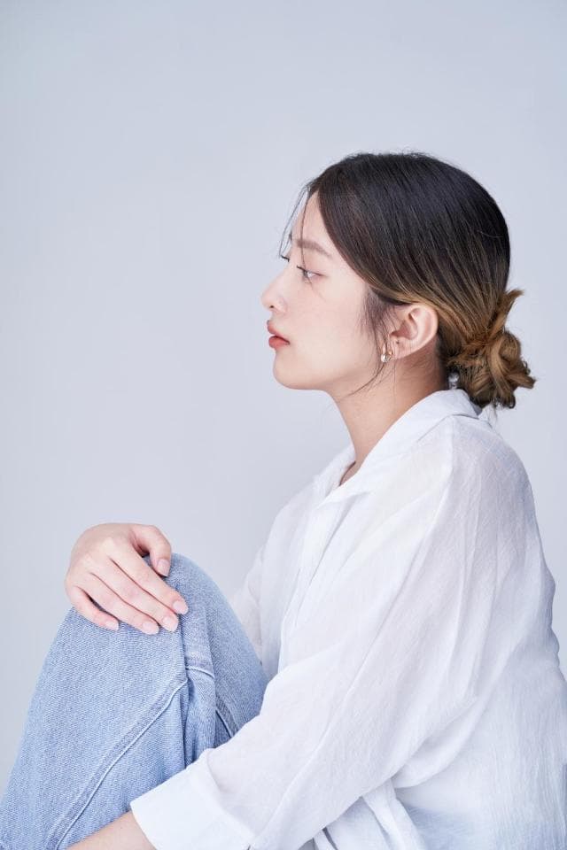 這張照片是一個穿著白色襯衫和牛仔褲的年輕女子,她的頭髮綁成一個髮髻,她正看著鏡頭。