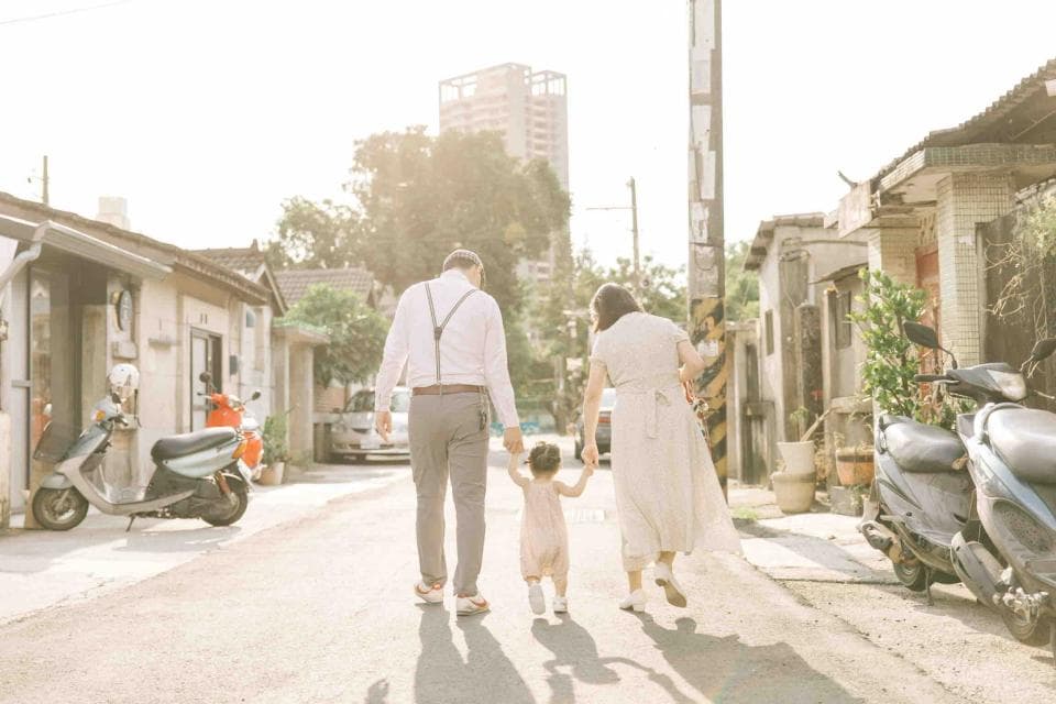 這張「一家三口走在巷弄裡」的照片是,爸爸牽著女兒,媽媽走在後面,一家三口走在陽光灑落的巷弄裡,畫面溫馨美好。