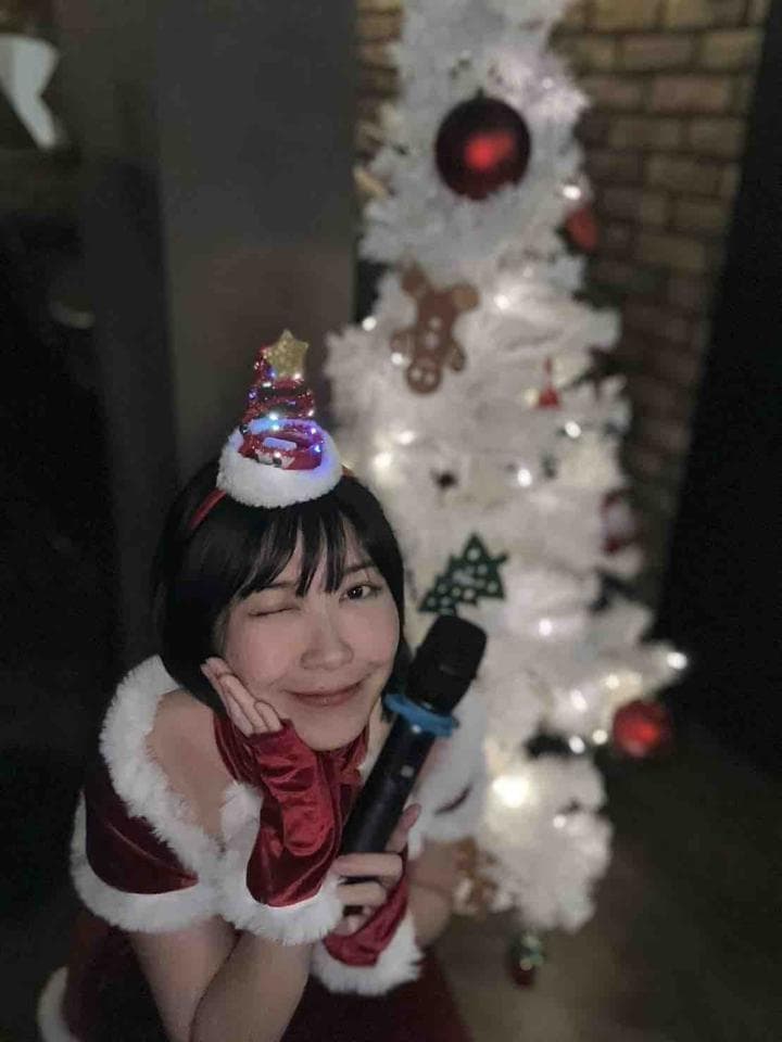 這張「聖誕節」的照片是一個戴著聖誕帽的女孩,她手裡拿著麥克風,背景是一棵白色聖誕樹。