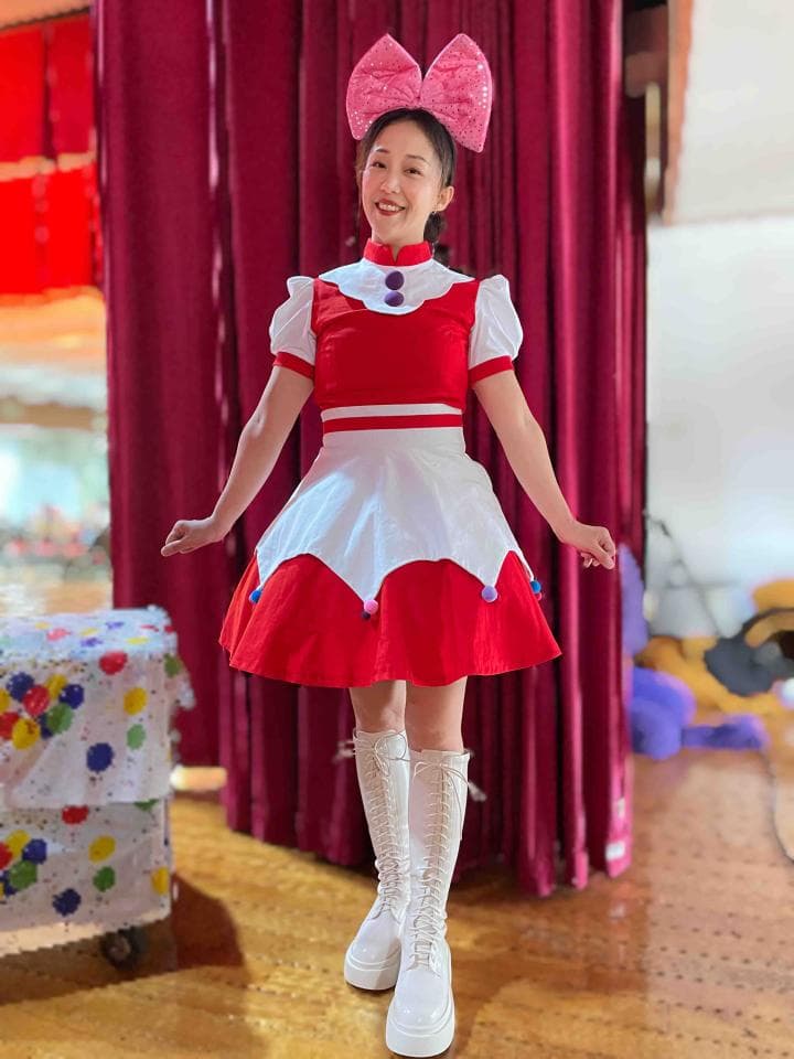 這張「一位女孩穿著紅白相間的蓬蓬裙,頭上戴著粉紅色蝴蝶結,在紅色的佈景前拍照」的照片是。