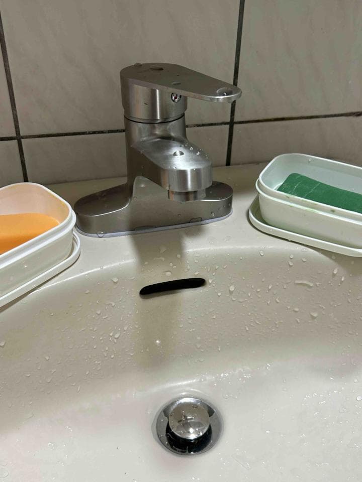 這張「浴室」的照片是 一個水槽、一個水龍頭和兩個小皂盒,水槽裡有水滴。