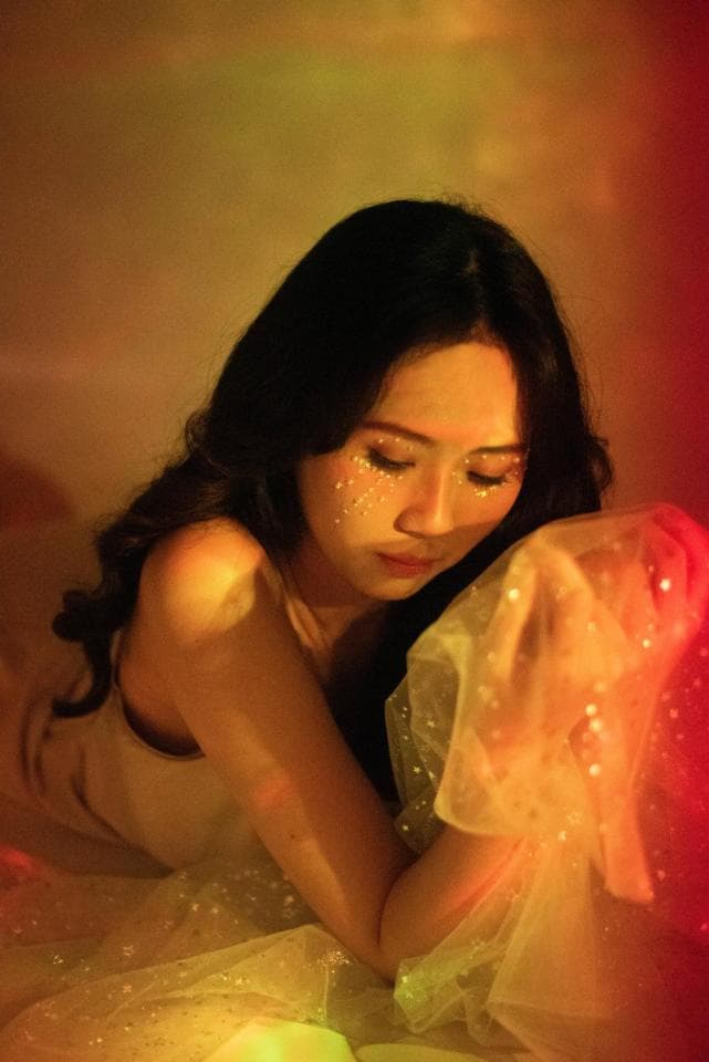 這張「一位年輕女子在燈光下低頭」的照片是,她穿著白色蕾絲衣服,右手握著蕾絲布料,散發著柔美氣質。