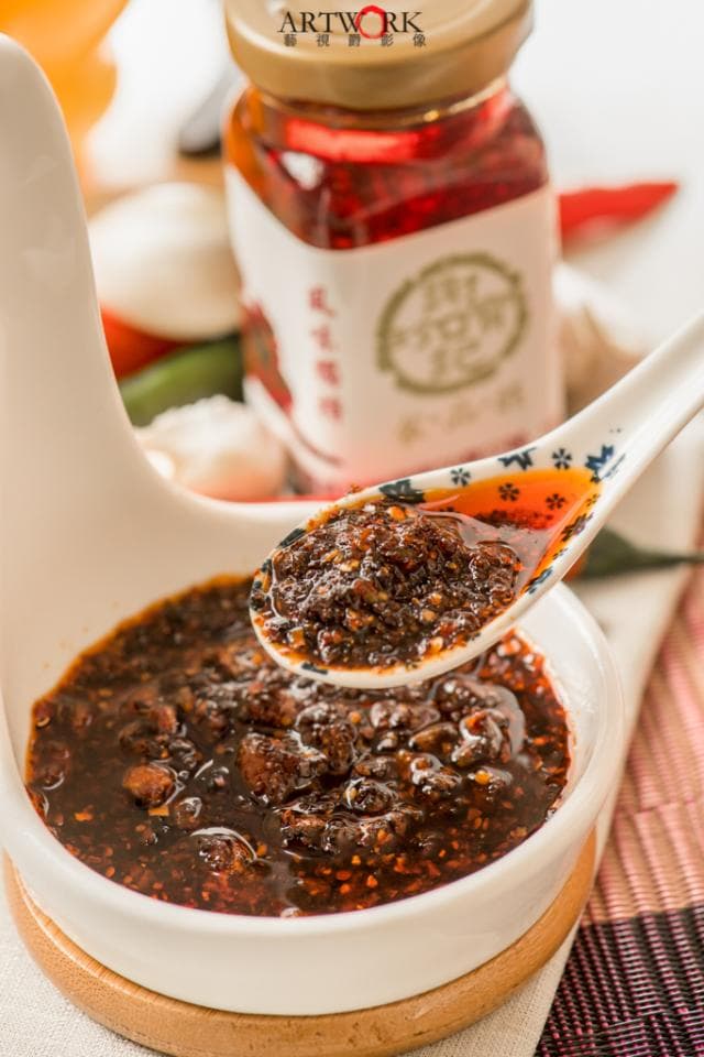 這張「辣椒醬」的照片是一碗裝滿辣椒醬的白色碗,還有一隻勺子舀起了一些辣椒醬。辣椒醬看起來很濃稠,有紅色的辣椒和黑色的芝麻。